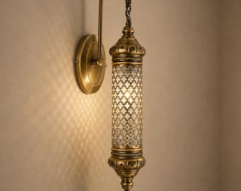 May include: A wall-mounted lamp featuring an antique brass finish and a cylindrical glass shade with a repeating diamond-shaped lattice pattern. The fixture includes a curved arm, a circular wall plate, and a decorative metal finial at the bottom.