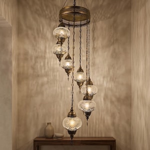 May include: An ornate, antique-style chandelier with multiple glass globes. The fixture has a bronze finish and is suspended from the ceiling. The glass globes have a textured pattern, and the light casts intricate shadows on the wall.