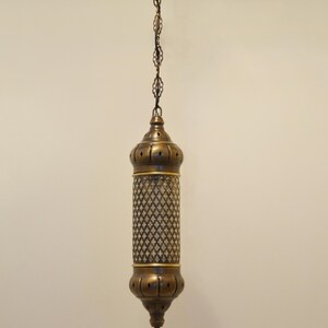 May include: A cylindrical brass pendant light fixture featuring a central mesh panel with a diamond pattern, capped by rounded brass ends with small cutouts, suspended from a matching brass chain and a decorative ceiling canopy.