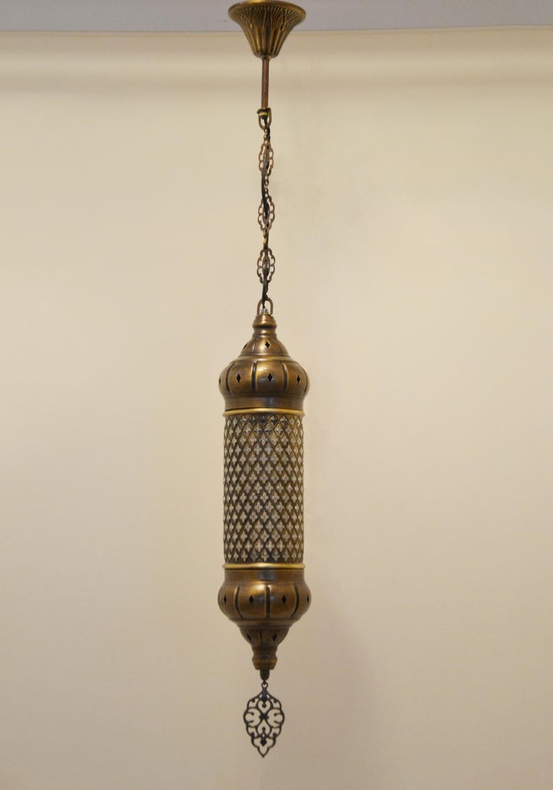May include: A cylindrical brass pendant light fixture featuring a central mesh panel with a diamond pattern, capped by rounded brass ends with small cutouts, suspended from a matching brass chain and a decorative ceiling canopy.