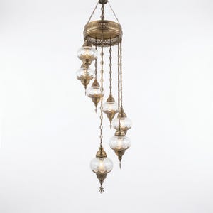 May include: An antique brass chandelier with eight clear glass globe shades. The fixture has an ornate design with intricate metalwork and hangs from a central canopy. The glass globes have a textured pattern, and the overall design is elegant.