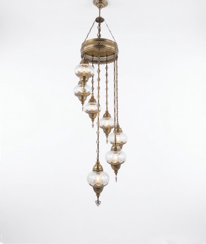 May include: An antique brass chandelier with eight clear glass globe shades. The fixture has an ornate design with intricate metalwork and hangs from a central canopy. The glass globes have a textured pattern, and the overall design is elegant.