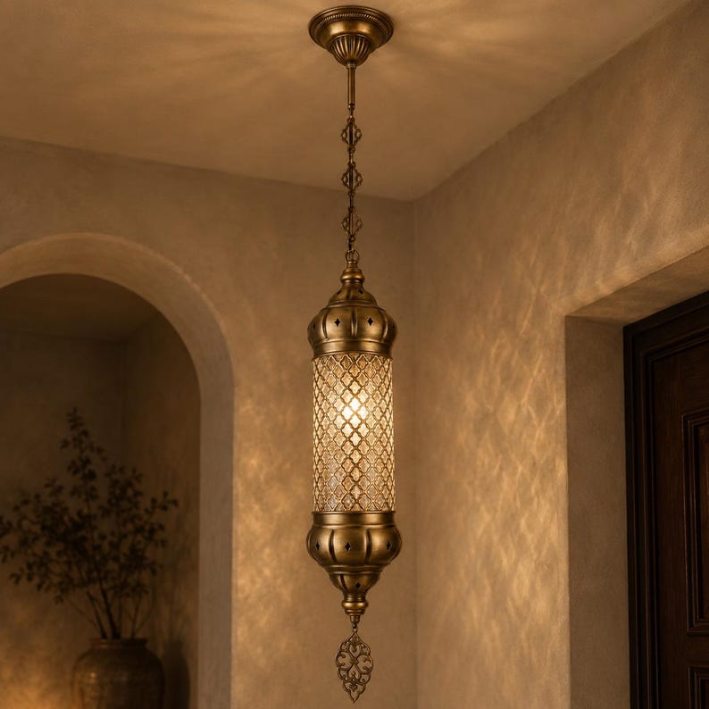 May include: A cylindrical pendant light fixture with an antique brass finish, featuring a central glass section with a diamond-patterned lattice overlay. The lamp hangs from a matching brass chain and includes a decorative metal finial.