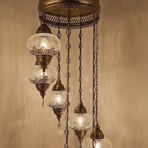 May include: An antique brass chandelier with six glass globe lamps. Each globe has a crackled texture and is suspended by decorative chains. The chandelier features intricate metalwork and a warm, inviting glow, perfect for adding a touch of elegance to any space.
