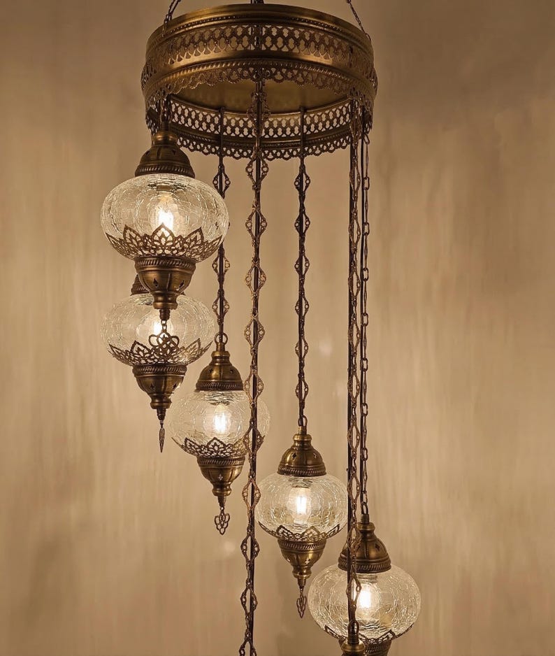 May include: An antique brass chandelier with six glass globe lamps. Each globe has a crackled texture and is suspended by decorative chains. The chandelier features intricate metalwork and a warm, inviting glow, perfect for adding a touch of elegance to any space.