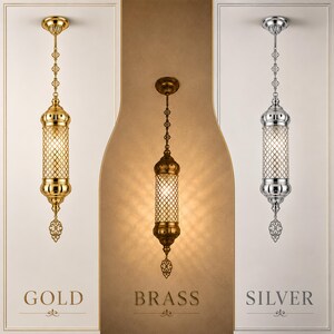 May include: Three cylindrical pendant lights hanging vertically. The left light is gold, the center is brass, and the right is silver. Each features a decorative metal lattice shade, a circular ceiling mount, and a filigree finial at the bottom.