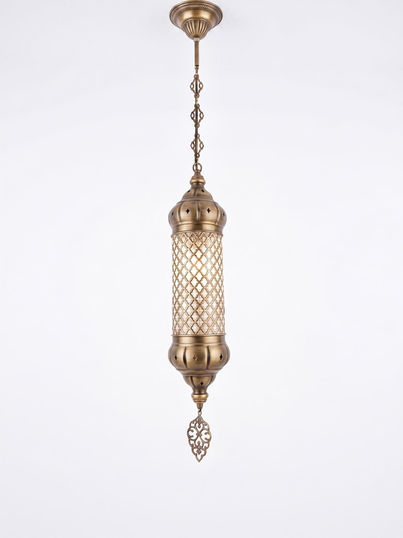May include: A cylindrical pendant light fixture with an antique brass finish. The central section features a clear glass panel with a diamond-shaped lattice overlay. It hangs from a matching brass ceiling canopy by a decorative chain.