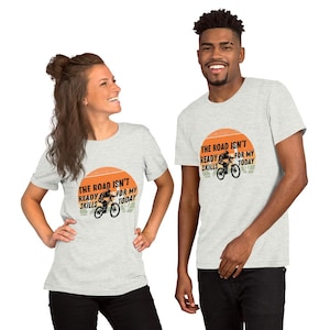 Op de afbeelding: Twee mensen dragen grijze T-shirts met een afbeelding van een mountainbiker en de tekst "The road isn't ready for my skills today".