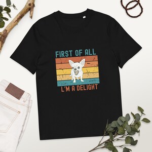 Op de afbeelding: Zwart T-shirt met een retro-grafische afbeelding van een chihuahua met de tekst "First of all, I'm a delight."