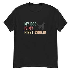 Op de afbeelding: Zwart T-shirt met een vintage-stijl grafische afbeelding met de tekst "Mijn hond is mijn eerste kind" met een silhouet van een hond.