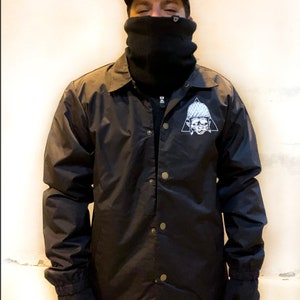 May include: A black nylon jacket with a snap closure and a white graphic of a skull wearing a helmet inside a triangle.