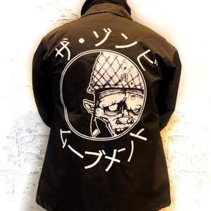 May include: Black jacket with a white circle graphic on the back. The graphic features a cartoon zombie wearing a military helmet and the text "ザ・ゾンビ・マーチ" in Japanese.