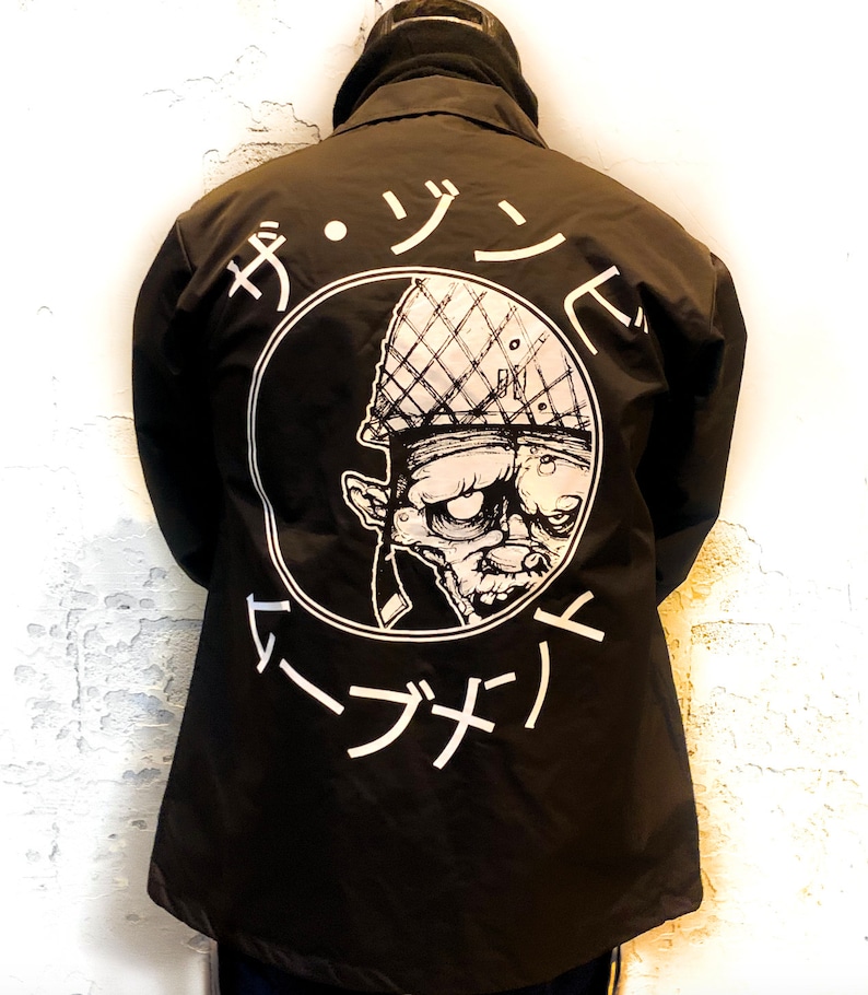 May include: Black jacket with a white circle graphic on the back. The graphic features a cartoon zombie wearing a military helmet and the text "ザ・ゾンビ・マーチ" in Japanese.