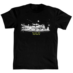 Puede incluir: Camiseta negra con una imagen en blanco y negro de un hombre en un coche. El texto "The eyes, chico. They never lie." está impreso en amarillo en la camiseta.