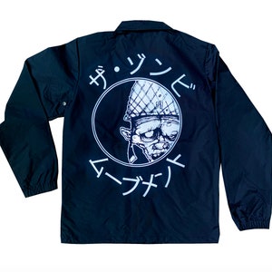 May include: Black coach jacket with a white circle graphic on the back. The graphic features a cartoon character wearing a helmet and the text "ザ・ゾンビ  マーナサイ".