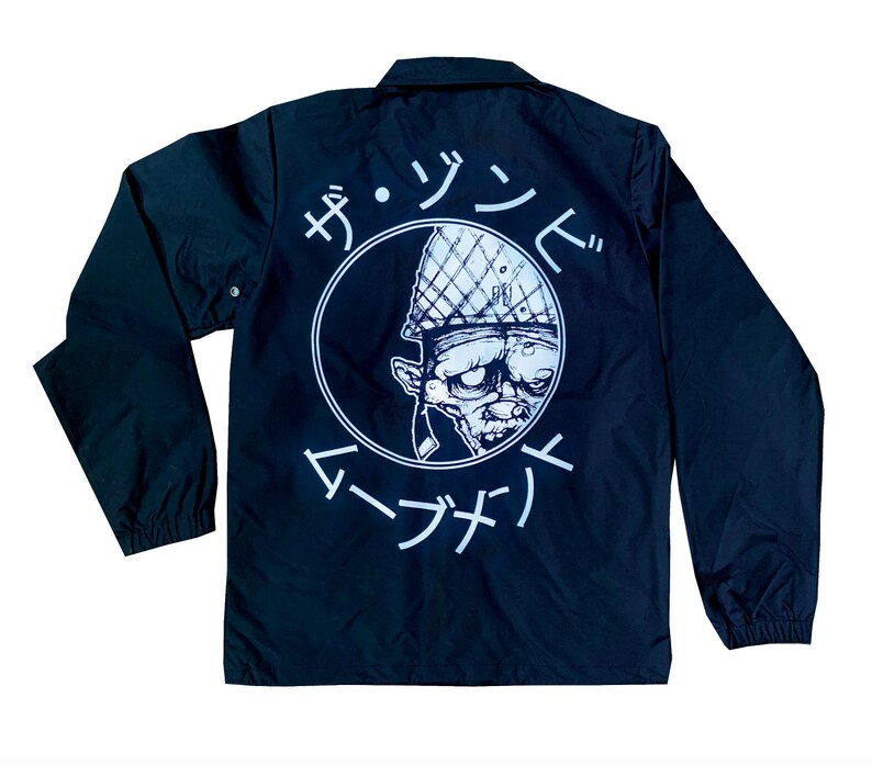 May include: Black coach jacket with a white circle graphic on the back. The graphic features a cartoon character wearing a helmet and the text "ザ・ゾンビ  マーナサイ".