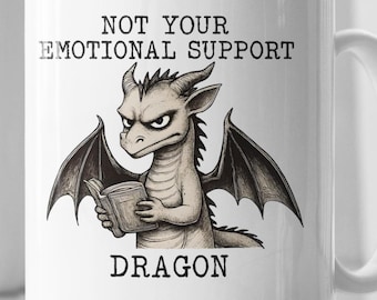 Puede incluir: Taza de cerámica blanca con una ilustración de un dragón sosteniendo un libro. El texto en la taza dice "NOT YOUR EMOTIONAL SUPPORT DRAGON". El dragón tiene una expresión severa y está representado con alas.