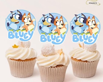 May include: Three cupcakes with blue and orange cartoon dog toppers. The toppers feature the characters Bluey and Bingo from the children's television show Bluey. The cupcakes are decorated with white frosting and sprinkles.