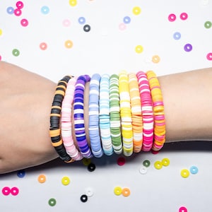 May include: A stack of colorful bracelets made of small, round beads. The bracelets are arranged in a rainbow pattern, with each bracelet featuring a different color combination.