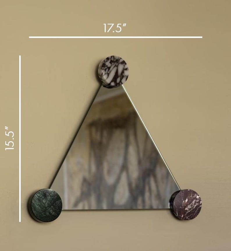 May include: A triangular mirror with a 17.5-inch width and 15.5-inch height. The mirror is accented with three circular marble pieces in shades of brown, green, and red. The mirror is mounted on a neutral-colored wall.
