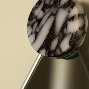 May include: A round, marble-like object with a black and white pattern. The object is attached to a clear, angled surface, possibly glass. The design is reminiscent of natural stone, with dark veining against a white background.