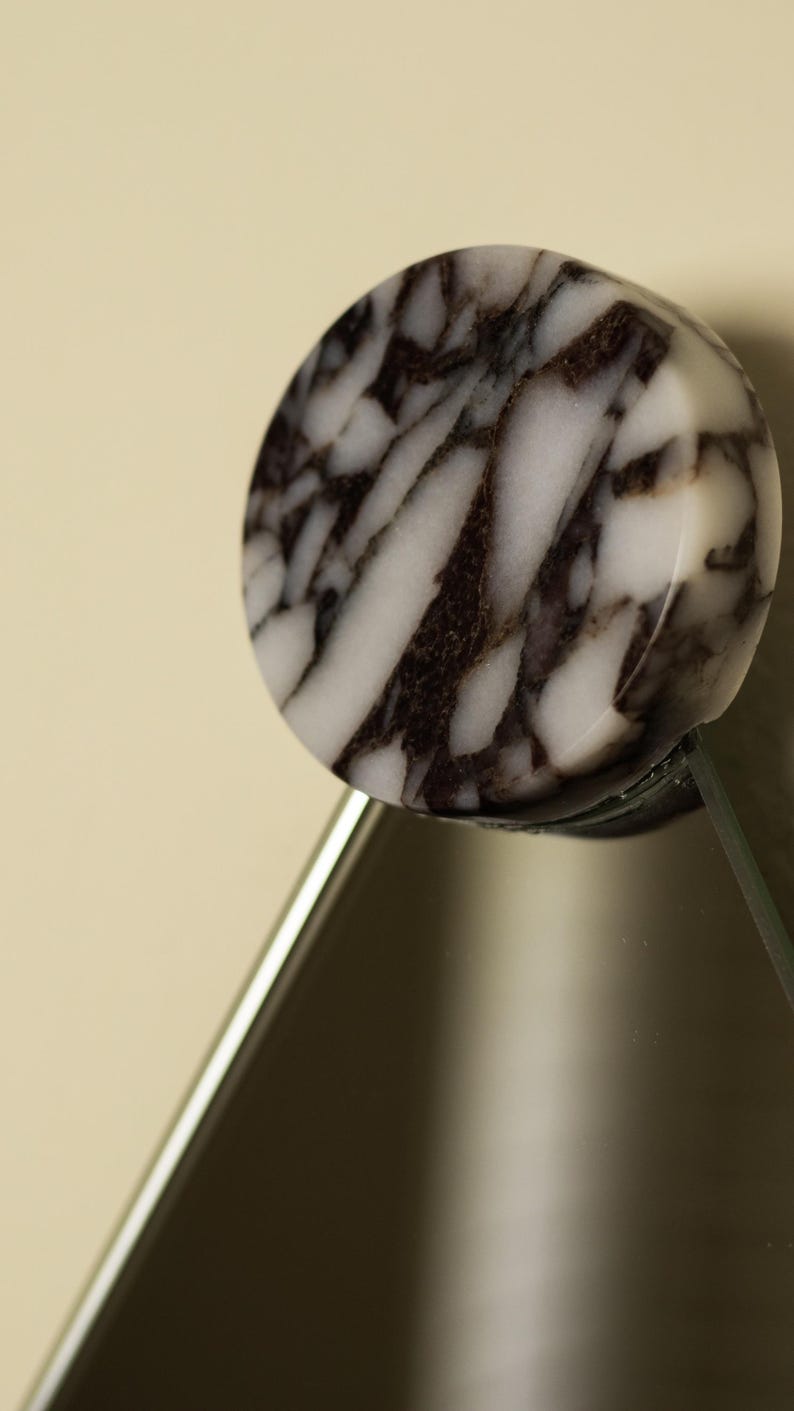 May include: A round, marble-like object with a black and white pattern. The object is attached to a clear, angled surface, possibly glass. The design is reminiscent of natural stone, with dark veining against a white background.