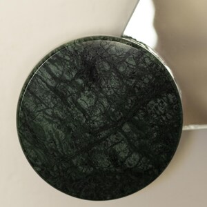 May include: A round, dark green marble object with intricate veining. The marble has a polished surface and is set against a neutral background. The object appears to be a decorative element or part of a larger design.