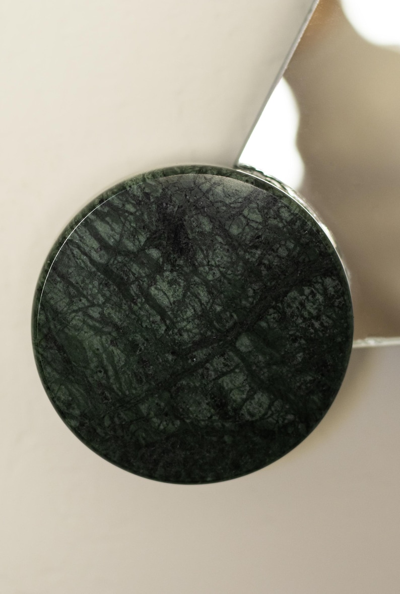 May include: A round, dark green marble object with intricate veining. The marble has a polished surface and is set against a neutral background. The object appears to be a decorative element or part of a larger design.