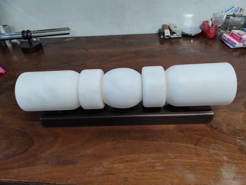 May include: A horizontal wall light fixture featuring a dark bronze rectangular base and five white, smooth, cylindrical and spherical glass shades arranged in a linear pattern, creating a balanced and geometric lighting design.