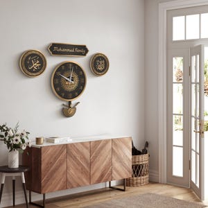 May include: A set of wall decorations including a clock and other pieces. The clock has a black face with gold detailing and a pendulum. Above the clock are three decorative items, one with the text "Mohammed Family". The items are mounted on a white wall.