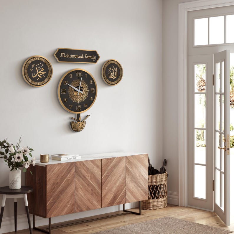 May include: A set of wall decorations including a clock and other pieces. The clock has a black face with gold detailing and a pendulum. Above the clock are three decorative items, one with the text "Mohammed Family". The items are mounted on a white wall.