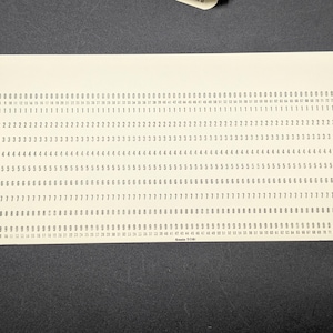 May include: A rectangular off-white vintage computer punch card featuring rows of printed numbers from zero to nine, with column numbers one through eighty printed at the top and bottom, and the text "Keele 7081" printed at the bottom center.