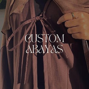 Può includere: Primo piano di un abaya personalizzato di colore marrone scuro. L'abaya presenta una chiusura con fiocco e un design a strati. Il testo "CUSTOM ABAYAS" è visualizzato in scrittura bianca.