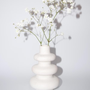 Può includere: Vaso in ceramica bianca con un design unico e stratificato. Il vaso è pieno di un bouquet di delicati fiori bianchi di gipsofila.