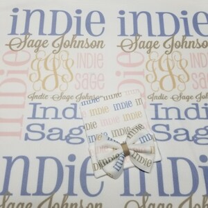 May include: A white baby blanket with the names "Indie Sage Johnson" repeated in a pattern. The blanket is paired with a white baby hat with a bow. The hat has the name "Indie" repeated in a pattern.