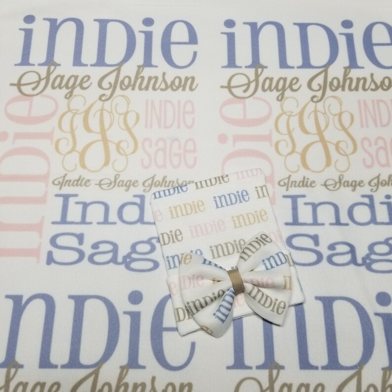 May include: A white baby blanket with the names "Indie Sage Johnson" repeated in a pattern. The blanket is paired with a white baby hat with a bow. The hat has the name "Indie" repeated in a pattern.