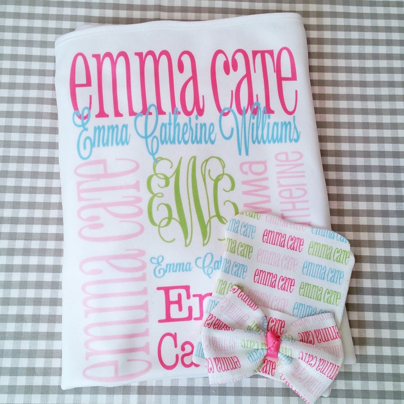 Puede incluir: Una manta de beb&eacute; blanca con el nombre "Emma Cate" impreso en rosa y azul. La manta tambi&eacute;n incluye el nombre "Emma Catherine Williams" impreso en una fuente m&aacute;s peque&ntilde;a. Se incluye un gorro y un lazo a juego.