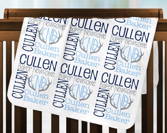 May include: A white baby blanket with a repeating pattern of the name "Cullen", the last name "Baker", and the middle name "Newsome" in navy blue and gray. The blanket also features a monogram with the initials "NB" and antler designs in light blue and gray.
