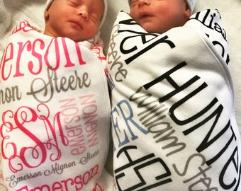 May include: Two newborn babies wrapped in personalised blankets. The girl's blanket is pink and white with the name "Emerson Mignon Steere" written in pink and black. The boy's blanket is white and blue with the name "Hunter William Steere" written in black and blue.