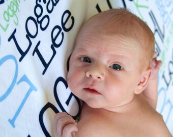 May include: A newborn baby boy lying on a white blanket with blue and green text that reads "Logan Lee Keller" and "Logan".