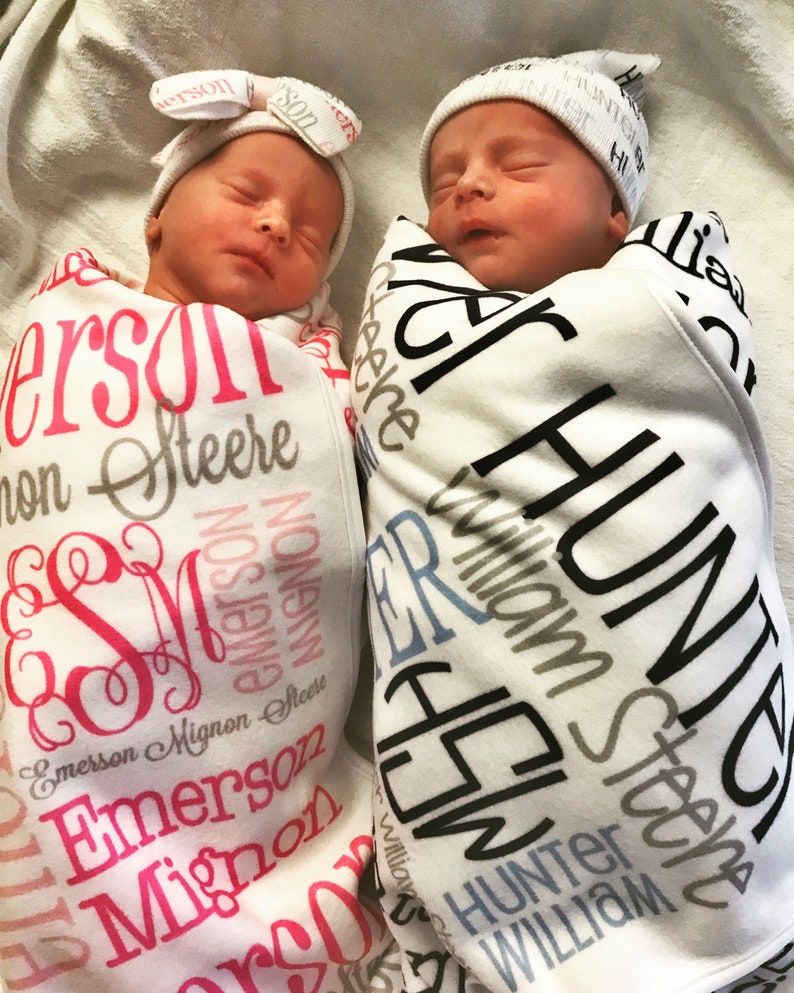 Puede incluir: Dos beb&eacute;s reci&eacute;n nacidos envueltos en mantas personalizadas. La manta de la ni&ntilde;a es rosa y blanca con el nombre "Emerson Mignon Steere" impreso en rosa y negro. La manta del ni&ntilde;o es blanca y azul con el name "Hunter William Steere" impreso en negro y gris.