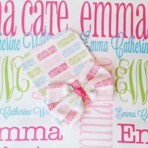 Puede incluir: Un gorro blanco para beb&eacute; con un lazo rosa. El gorro est&aacute; cubierto con un patr&oacute;n repetido de los nombres "Emma Care" en rosa, azul y verde.