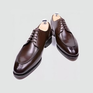 Op de afbeelding: Een paar bruine leren veterschoenen met een spitse neus en een lage hak.