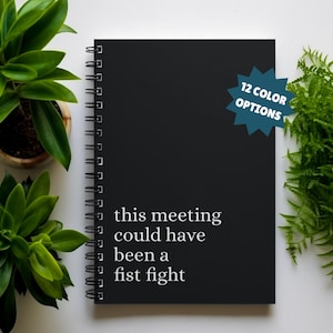 Puede incluir: Cuaderno negro de espiral con el texto "this meeting could have been a fist fight" en letras blancas. El cuaderno tiene una pegatina azul en forma de estrella con el texto "12 COLOR OPTIONS".