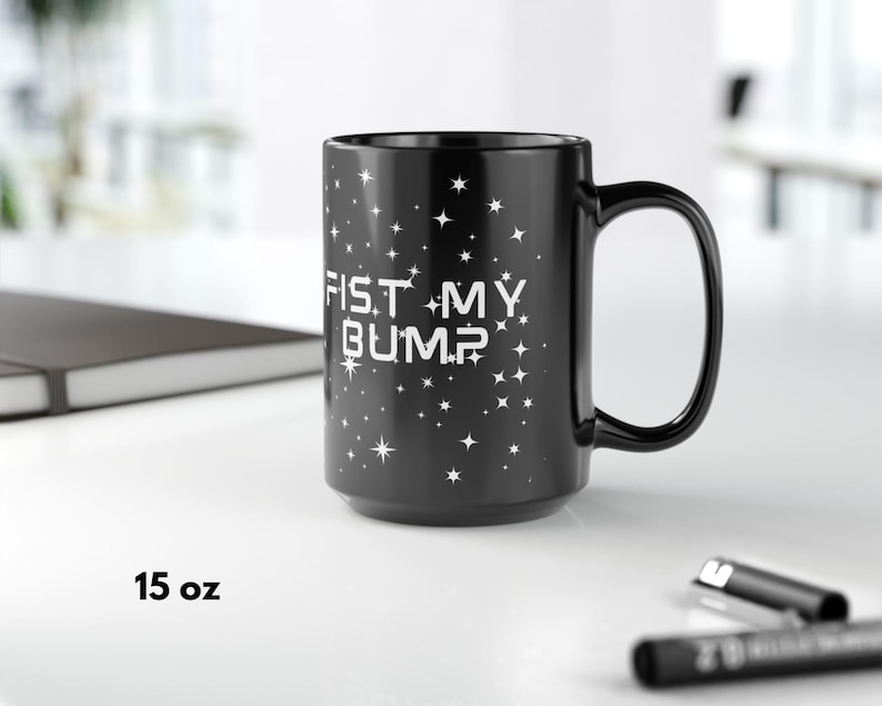 May include: Black 15 oz coffee mug with the text "FIST MY BUMP" in white, surrounded by white stars. The mug has a large handle and is on a white surface.