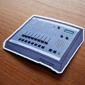 May include: A sticker featuring a gray and blue audio mixer. The mixer has sliders, buttons, and a display. The sticker is on a wooden surface. The sticker has the text "F-800" and "Free Systems Inc."