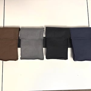 May include: Four rectangular fabric pouches in brown, gray, black, and navy blue, each featuring a top flap closure. These pouches are attached to a wide black webbing belt that runs horizontally behind them, providing a secure mounting system.