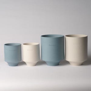 May include: Four ceramic planters in two different sizes and colors. Two planters are light blue and two are off-white. The planters are all cylindrical with a slightly flared base. The word "Earthenware" is embossed on each planter.