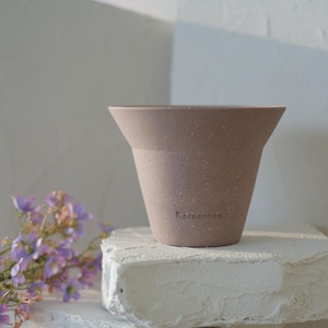May include: A light brown ceramic planter with a speckled finish. The planter has a wide mouth and a narrow base. The word "Karneteen" is printed on the side of the planter.