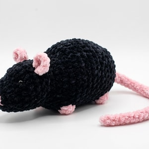Puede incluir: Un juguete de peluche hecho a mano con forma de rata negra con detalles rosas. La rata tiene un cuerpo redondeado, una larga cola curvada y pequeñas orejas y patas rosas. Hecho de material suave y texturizado.